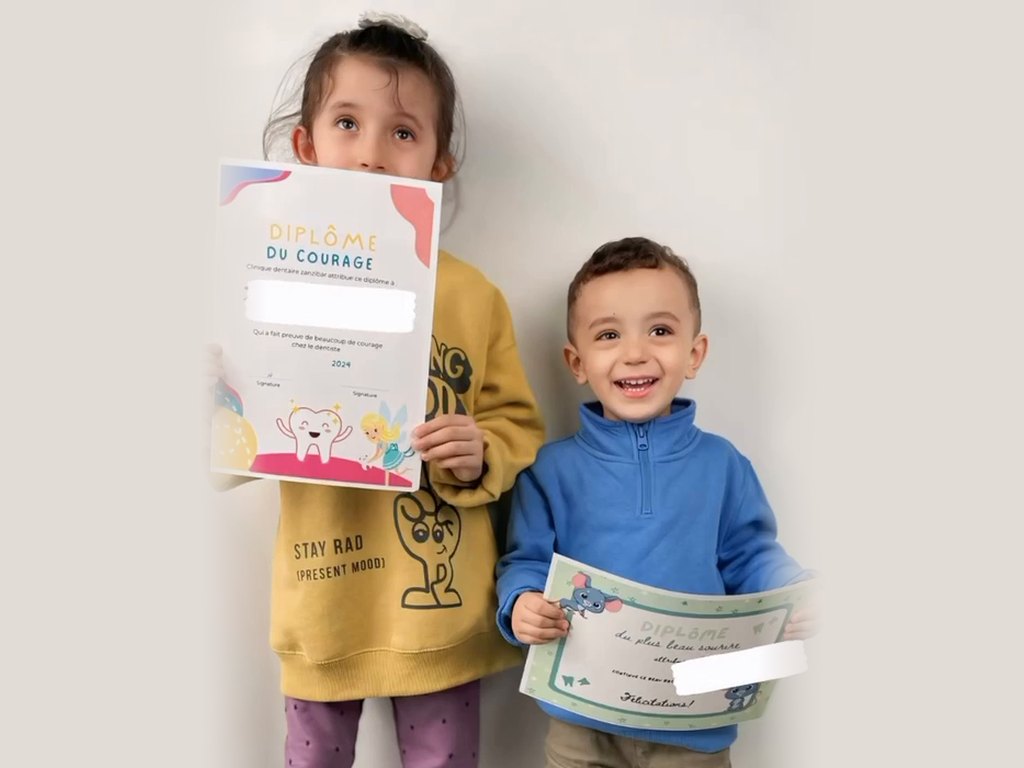 Deux enfants fiers de montrer leurs diplômes, le « Diplôme du courage » et le « Diplôme du plus beau sourire »